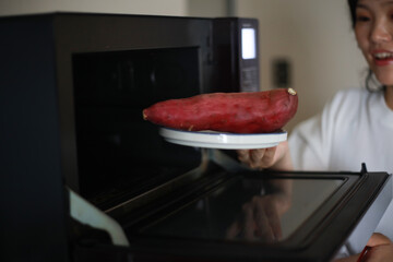 電子レンジでサツマイモを温めようとする女性