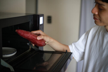 電子レンジでサツマイモを温めようとする男性