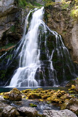 Fototapeta na wymiar Schöner verzweigter Wasserfall stürzt über Felsen herunter mit nassen Steinen im Vordergrund
