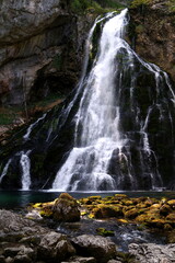 Schöner verzweigter Wasserfall stürzt über Felsen herunter mit nassen Steinen im Vordergrund