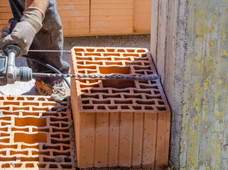 Anchoring of the masonry in the pillar for the anti-seismic prescription. With an electric drill, the hole for anchoring the steel bar to the reinforced concrete structure is made
