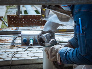 Worker is using electric wheel grinding on steel pipe structure in factory.