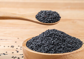 Close-up macro shot wooden spoon to scoop black sesame seeds from a wooden bowl on table wood background, organic  food concept.