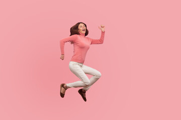 Fototapeta na wymiar Extremely happy satisfied woman with brown hair jumping high or flying in air, dreams comes true. Indoor studio shot isolated on pink background