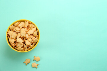 Delicious goldfish crackers in bowl on turquoise background, flat lay. Space for text
