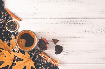 Cup of black  coffee, autumn yellow maple leaves, cones, cinnamon sticks, dried rose on a brown   blanket on a white wooden top view
