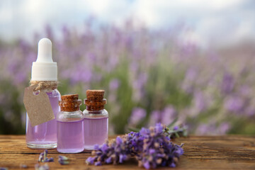 Obraz na płótnie Canvas Bottles of natural essential oil and lavender flowers on wooden table, closeup. Space for text