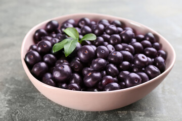 Tasty acai berries and green leaves in bowl on grey table, closeup