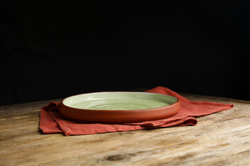 Empty plate and napkin on wooden table against black background