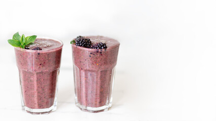 Fototapeta na wymiar Delicious blackberry smoothie with mint and fresh berries in glasses on white kitchen desk and white background, copy space