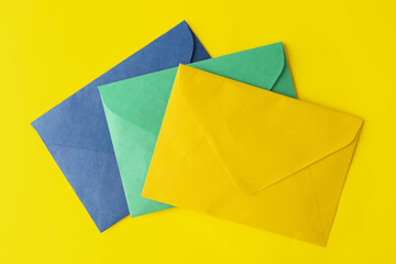 Colorful paper envelopes on yellow background, top view