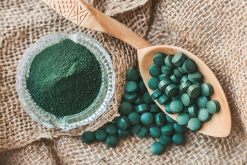 Pressed tablets, spirulina seaweed pills on a wooden spoon lying on an old burlap, detox food