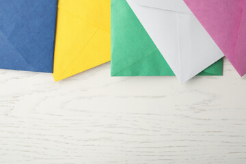 Colorful paper envelopes on white wooden background, flat lay. Space for text