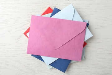 Colorful paper envelopes on white wooden background, top view