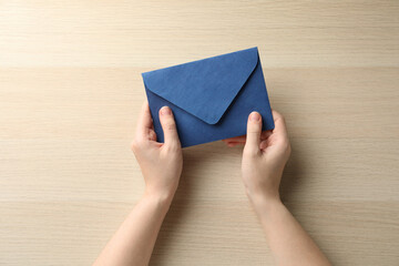 Woman with blue paper envelope at wooden table, top view