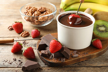 Fondue pot with chocolate and different products on wooden table