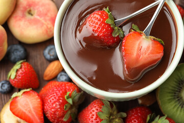 Fondue forks with strawberries in bowl of melted chocolate on table, flat lay