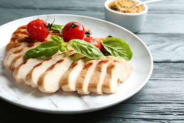 Tasty grilled chicken fillet with green basil and tomatoes on grey wooden table, closeup