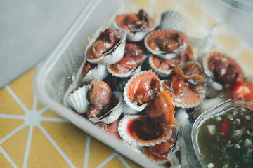 Boiled cockles with hot and spicy seafood sauce in box. Local menu from sea shell. Semi-cooked raw food