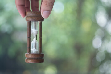 Man hand holding wooden hourglass against nature background.
