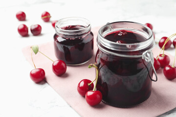 Jars of pickled cherries and fresh fruits on table, closeup