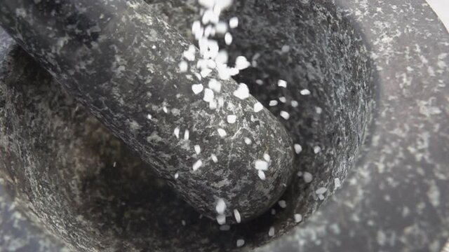 Large pieces of the sea salt are falling into the grey stone mortar in slow motion