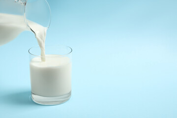 Pouring milk into glass on light blue background. Space for text