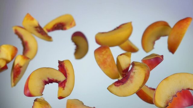 Slices of the fresh ripe peach are bouncing on the white background in slow motion