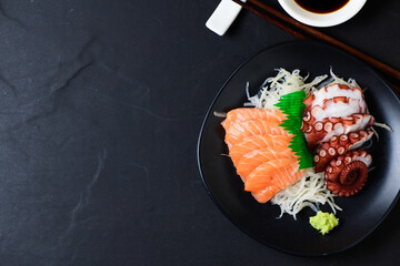 Salmon and Tako sashimi on black dish with chopsticks,