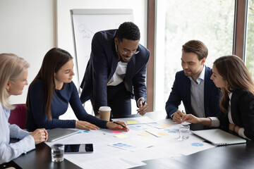 Multiethnic colleagues gather in boardroom brainstorm analyzing company financial paperwork together. Motivated diverse employees businesspeople talk discuss business project at team office meeting.