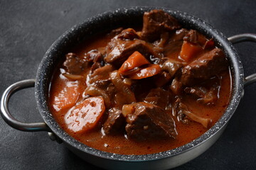 Beef Bourguignon in a pan. Stew with red wine ,carrots, onions, garlic, a bouquet garni, and garnished with pearl onions, mushrooms and bacon. French cuisine- regional recipe from Burgundy