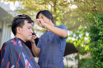Asian man making haircut and salon business at home. Outdoor barbershop in garden. Social...