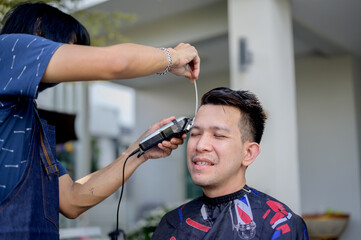 Asian man making haircut and salon business at home. Outdoor barbershop in garden. Social...