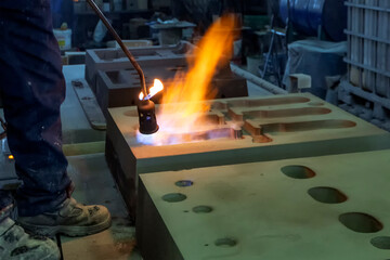 The worker is preheating to mold for casting.  Sand casting, also known as sand molded casting, is...