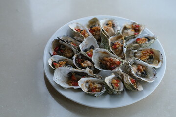 close up a plate of grilled oysters with spice on white table.