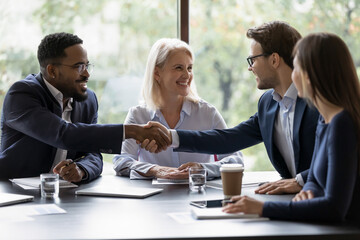 Smiling diverse businesspeople shake hands get acquainted greeting at team meeting in office. Happy multiracial male colleagues employees handshake at briefing with coworkers. Acquaintance concept. - Powered by Adobe