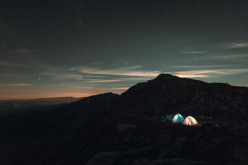 Two lighted tents on the mountain base in night