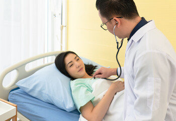 Fototapeta premium doctor using stethoscope to listen to lung and heart sound of asian woman pateint who is sick and lying in hospital bed. healthcare and medical concept