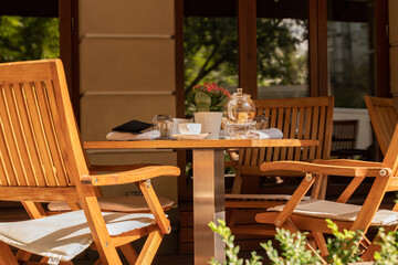 Empty chairs and tea utensils on the table of an open cafe or restaurant on Sunny summer day.
