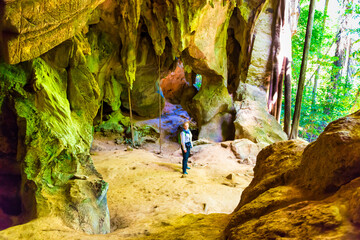 People in big dark cave- silhouette of woman in cave and sun light from jungle forest
