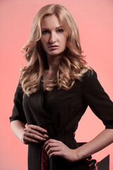 Fototapeta premium Slender strict blonde in black clothes on a pink background