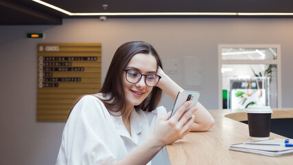 student girl is sitting at a table and using an app on her smartphone.