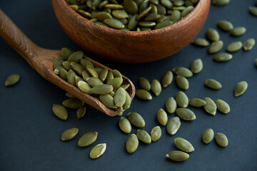pumpkin seeds in a wooden bowl and vintage scoop. Close up on a black background. copy space for text