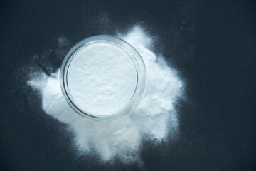 Glass bowl of baking soda. Spoonful of bicarbonate. Top view, flat lay. Close up on a black...