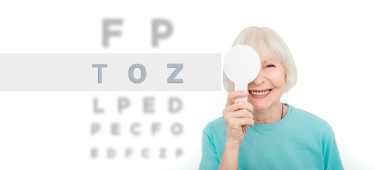 Senior woman having an eye exam with one eye covering using a special tool, on a white background. Eye test elderly patient © Peakstock