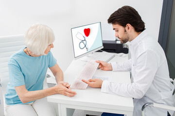 Cardiologist analyzes the electrocardiogram results of senior woman, close-up. Diagnosis of arrhythmia, heart rate, and heart disease