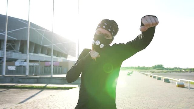 Front view of serious confident hardworking active bearded boxer in black mask and black sportswear which doing boxing punches outdoors