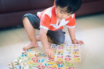 Asian little boy playing with wooden letter puzzle sitting on the floor at home, early education and leaning.