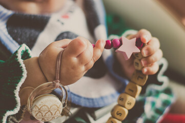 Las manos de un bebé sujetando una cadena de chupete en colores rosas
