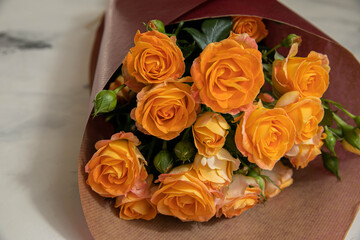 A festive bouquet of yellow-orange roses is Packed in Burgundy paper on a marble background
